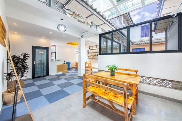 A spacious room with a wooden dining table, a potted plant, and a checkered floor.