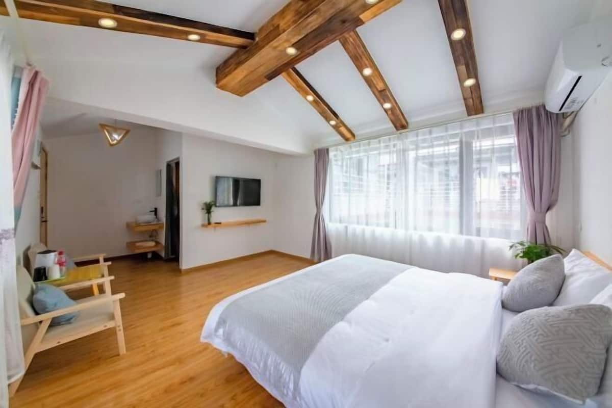 A bedroom with a large bed, wooden beams on the ceiling, a TV, and a window with curtains.