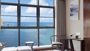 Une pièce dotée d’une grande fenêtre donnant sur la mer, d’une table avec des chaises et d’un lit simple.