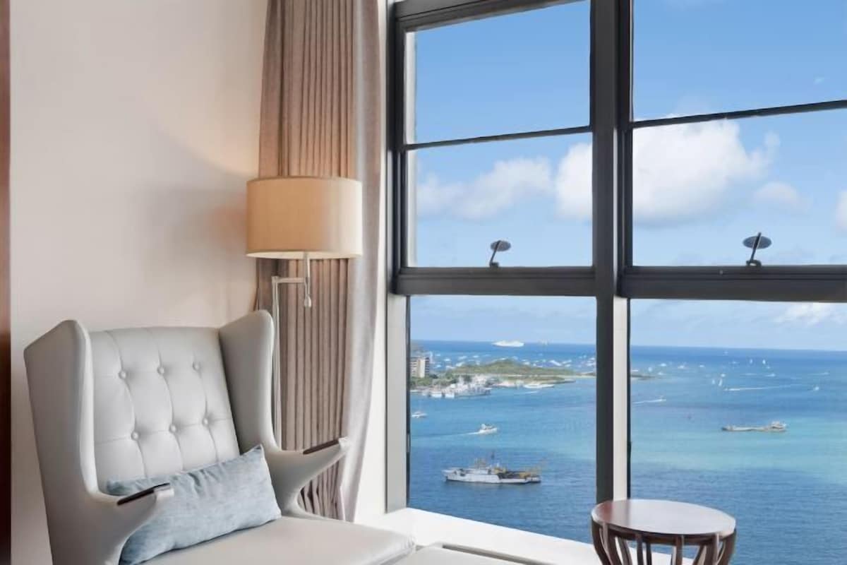 A room with a large window offering a view of the sea and boats.
