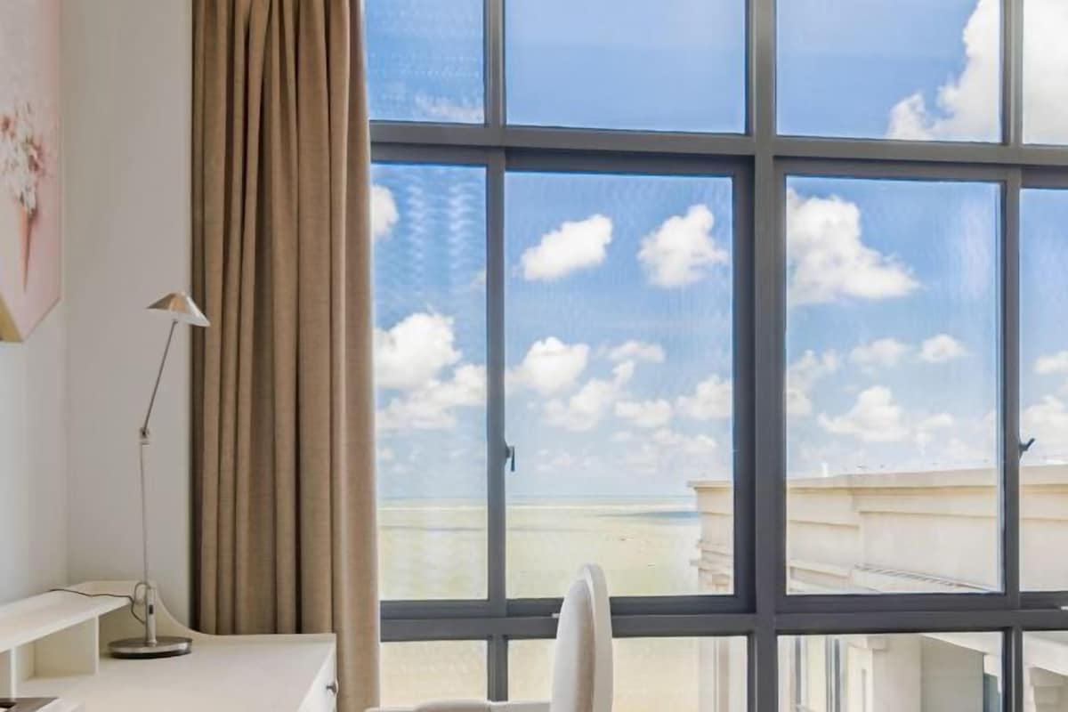 A room with a large window, a desk, a chair, and a lamp.