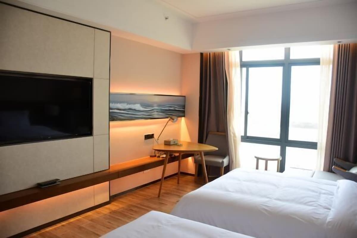 A hotel room with a bed, a desk, a TV, and a window with curtains.