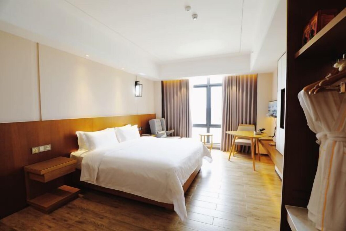 A hotel room with a large bed, bedside table, desk, chair, and a wardrobe.