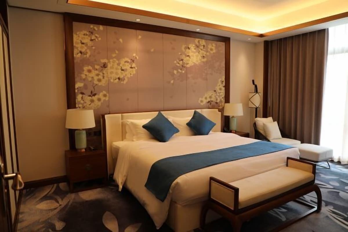A hotel room with a large bed, bedside tables, a chair, and a decorative wall panel.