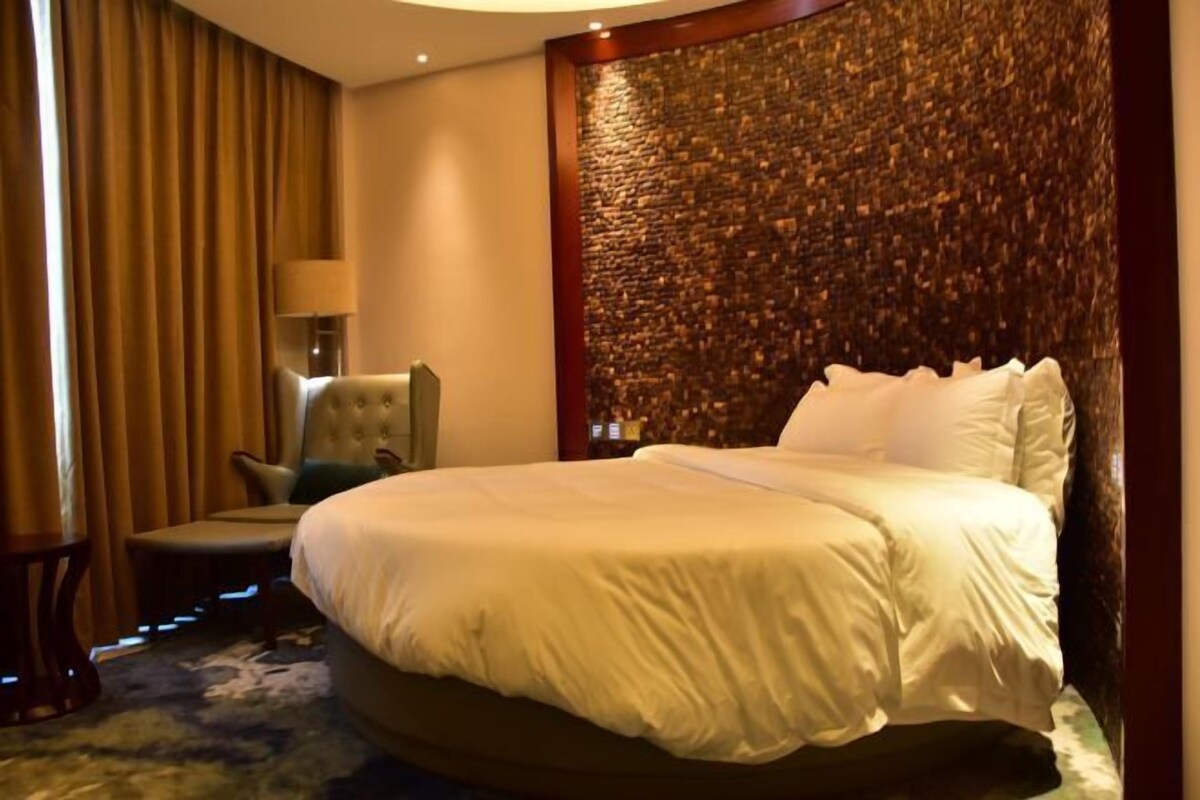 A hotel room with a large bed, a chair, a lamp, and a textured wall.