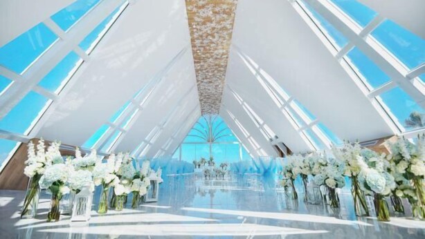 Un intérieur moderne avec un plafond haut et de grandes fenêtres, agrémenté d’une allée centrale décorée de compositions florales.