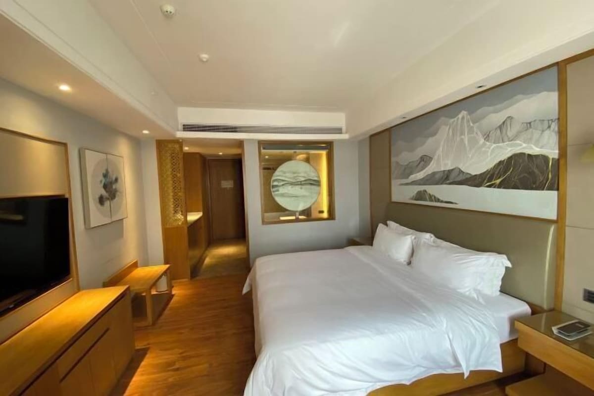 A modern hotel room with a large bed, a flat-screen TV, a painting on the wall, and a wooden floor.