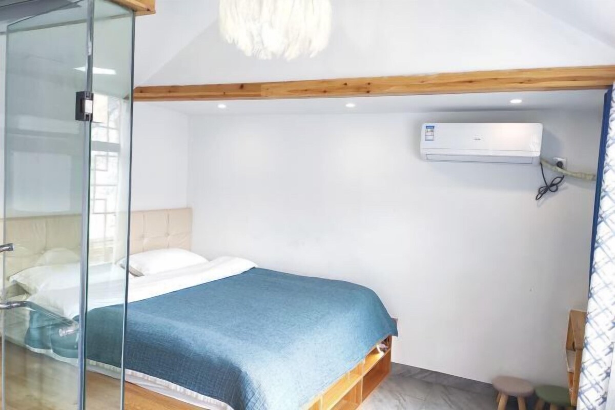 A bedroom with a bed, a glass shower enclosure, a wooden ceiling beam, and an air conditioning unit.