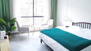 Ein modernes Hotelzimmer mit einem großen Bett, einem Schreibtisch und einem Stuhl. Ein Fenster mit grünen Vorhängen bietet einen Blick auf die äußere Bebauung.