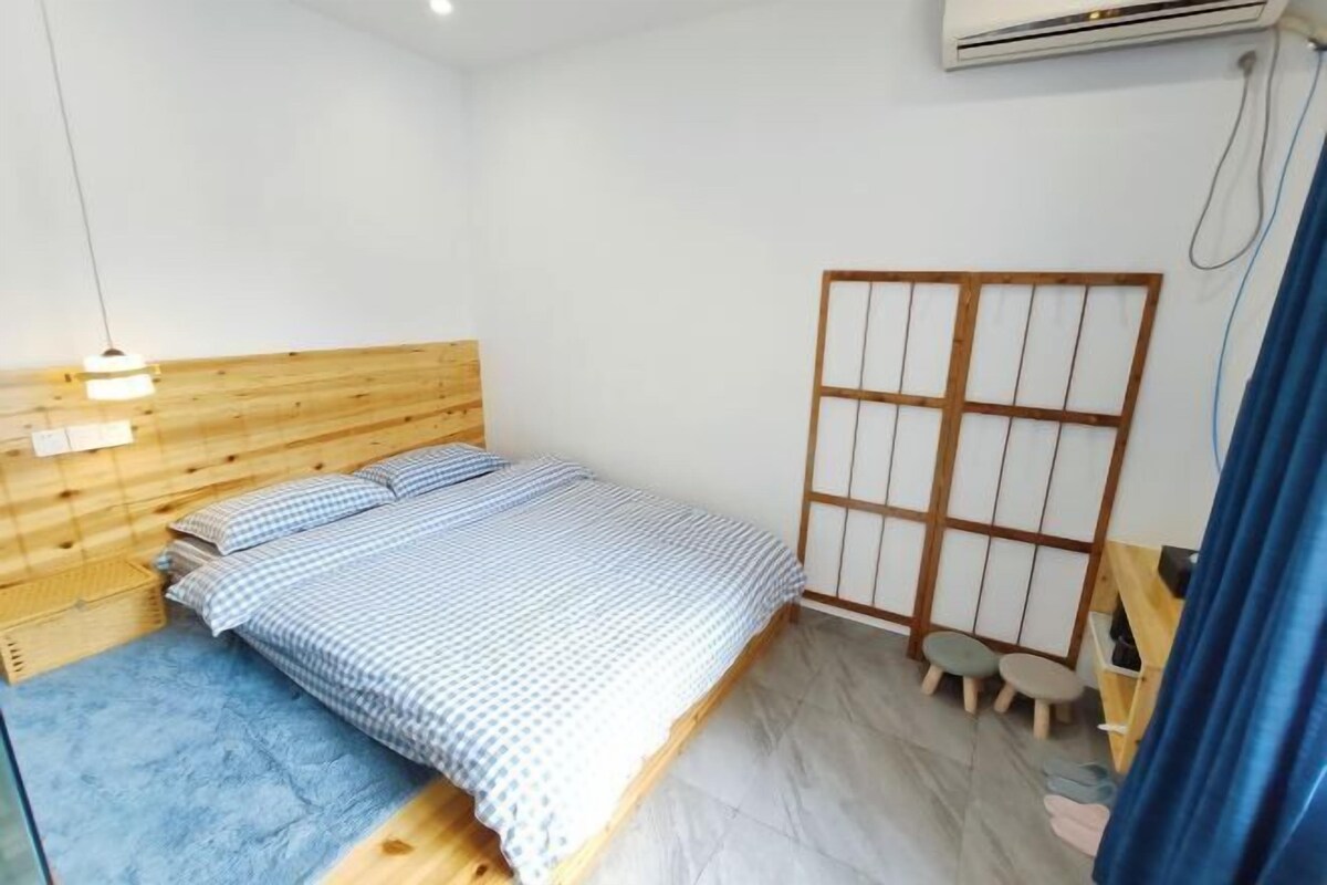 A bedroom with a wooden headboard, a bed with a checkered bedspread, a small stool, and a futon bed.