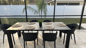 A rectangular outdoor table with four chairs, each with a woven placemat, and a potted plant in the center. - The Ultimate Escape (Palm Coast)