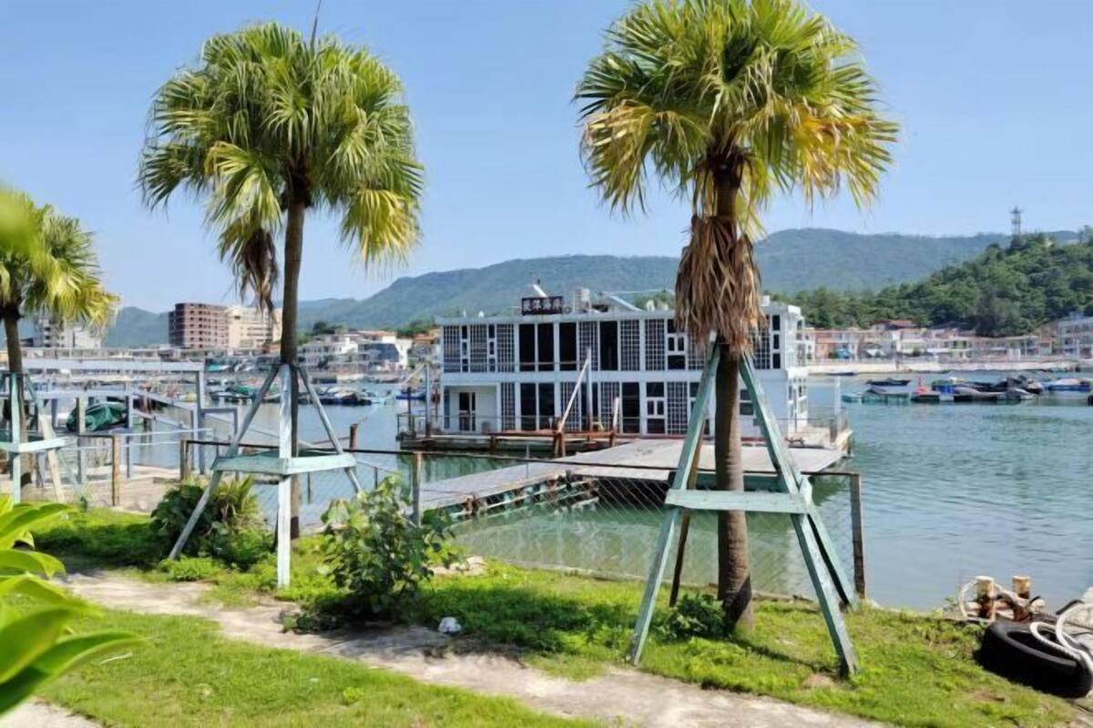 A waterfront property with a dock, palm trees, and a view of the cityscape.