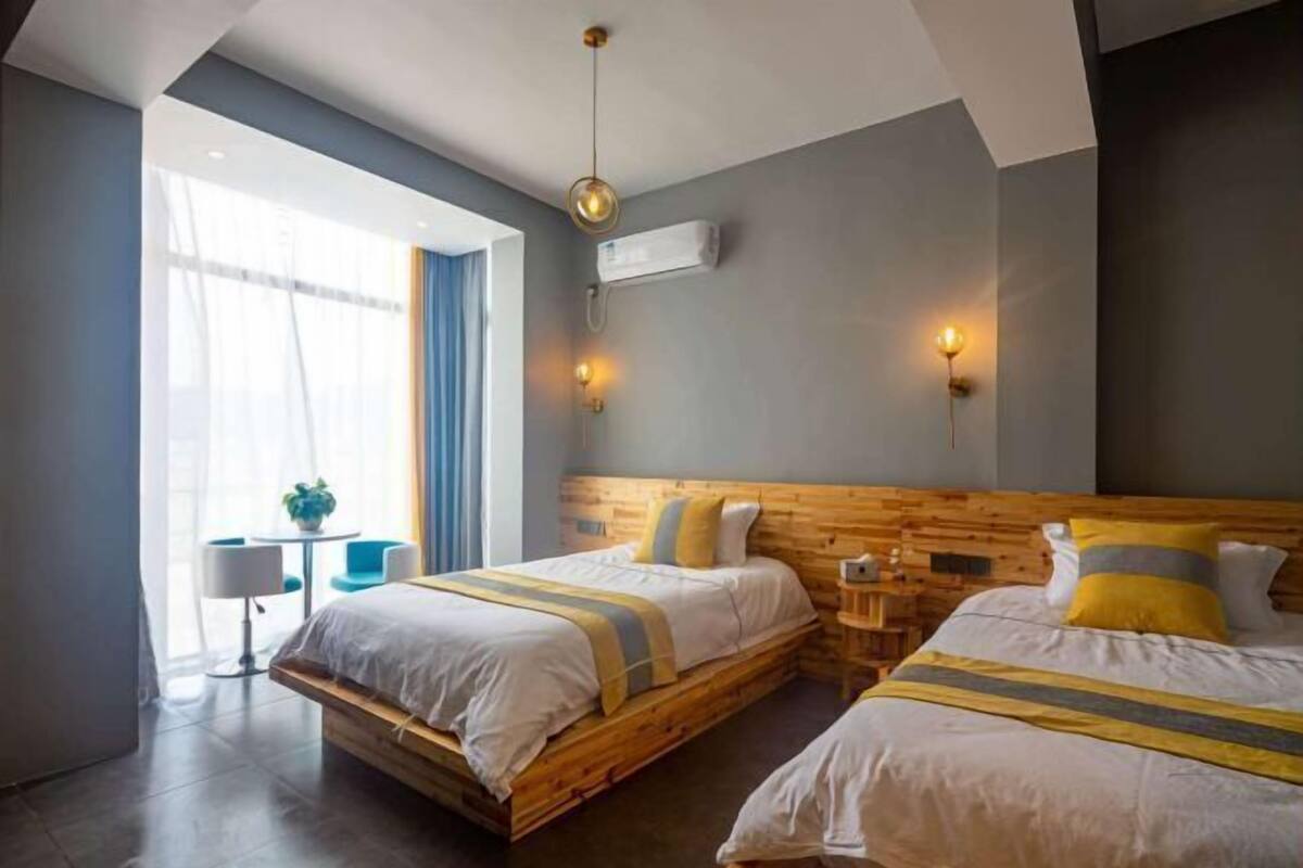 Ein Hotelzimmer mit zwei Betten, einem kleinen Tisch, einem Stuhl und einem Fenster mit Vorhängen.