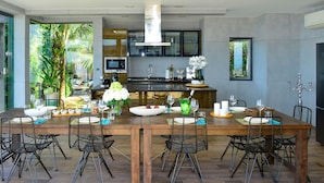A modern kitchen with a central island, large windows, and a dining area with chairs and a table set for six. - Paradise Villa Elysium (Koh Samui)