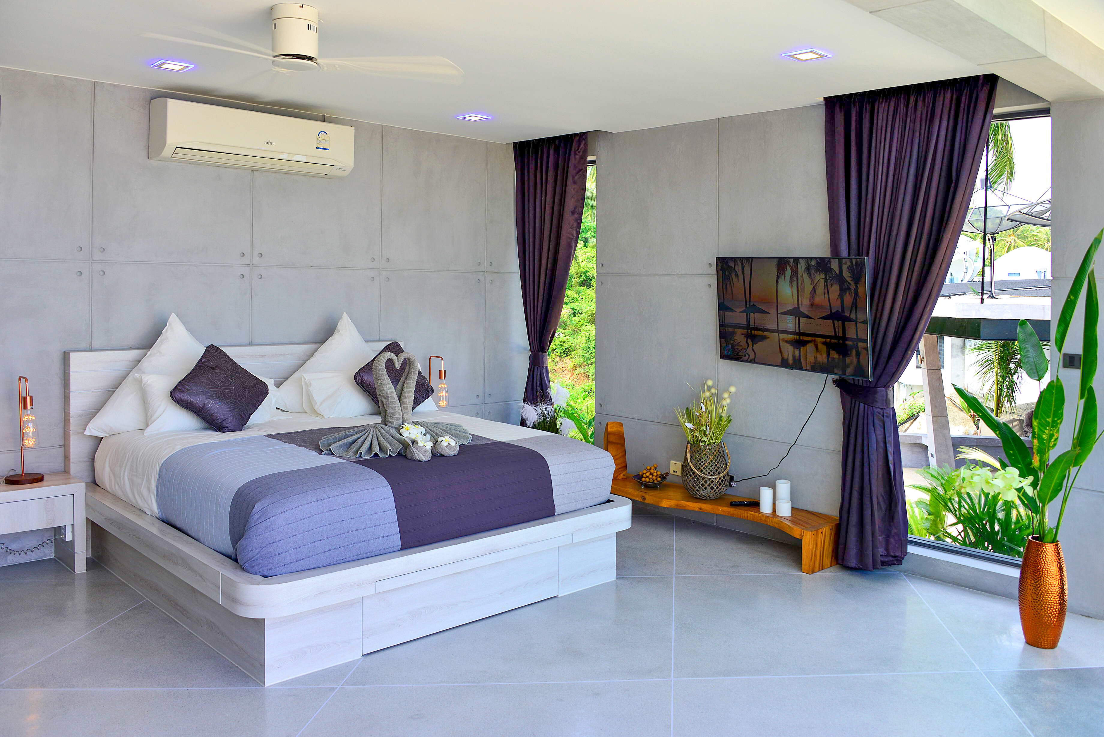 A modern bedroom with a large bed, a mounted TV, and a potted plant.