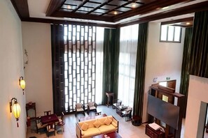 A spacious living area with a sofa, coffee table, and a fireplace. There is a large window with curtains, a decorative wall panel, and a seating area with chairs. - Gujian Yunhai Hotel (Chongqing)