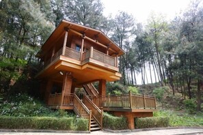 A wooden cabin with a balcony and stairs, surrounded by trees. - Gujian Yunhai Hotel (Chongqing)