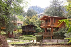 Una cabaña de madera con balcón, rodeada de árboles y un pequeño jardín.