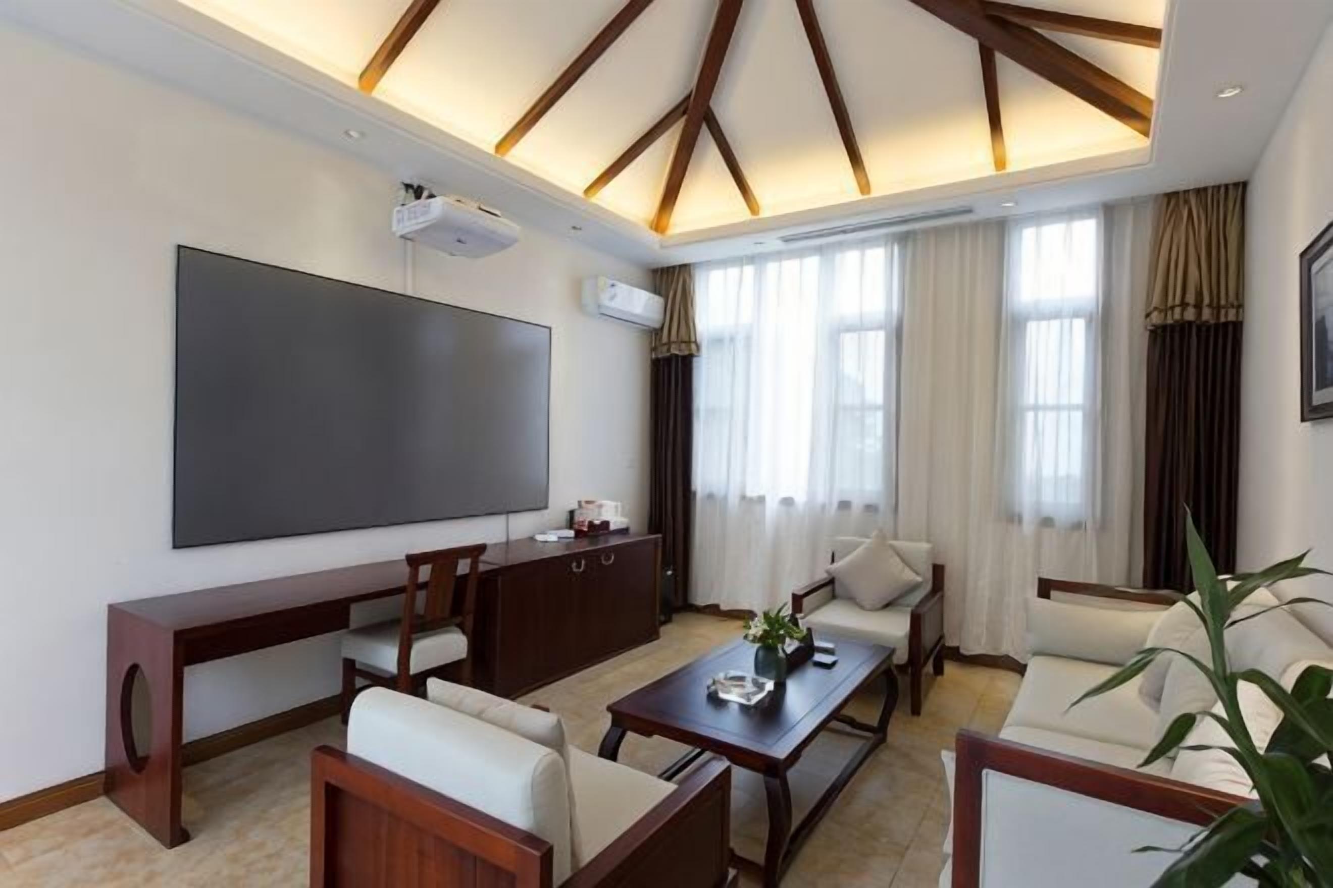 A modern living room with a flat-screen TV, wooden furniture, and large windows.