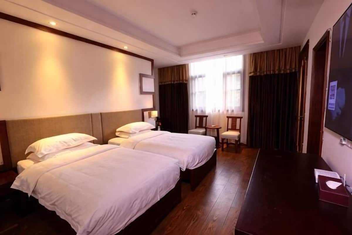 Une chambre d’hôtel avec deux lits, un bureau, une chaise et une grande fenêtre avec des rideaux.