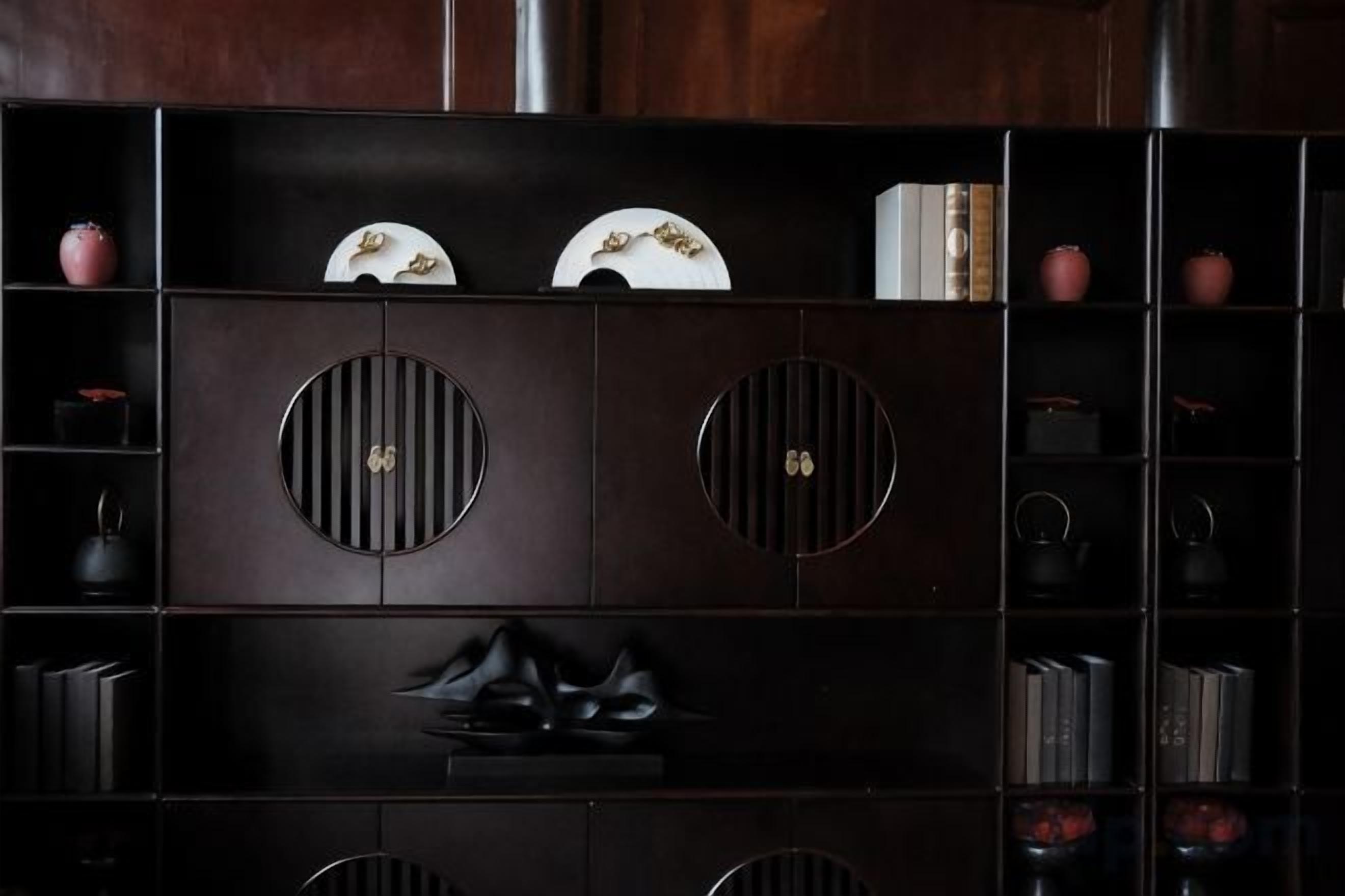A dark wooden cabinet with circular cutouts, shelves with books and decorative items, and a pair of black shoes on the lower shelf.