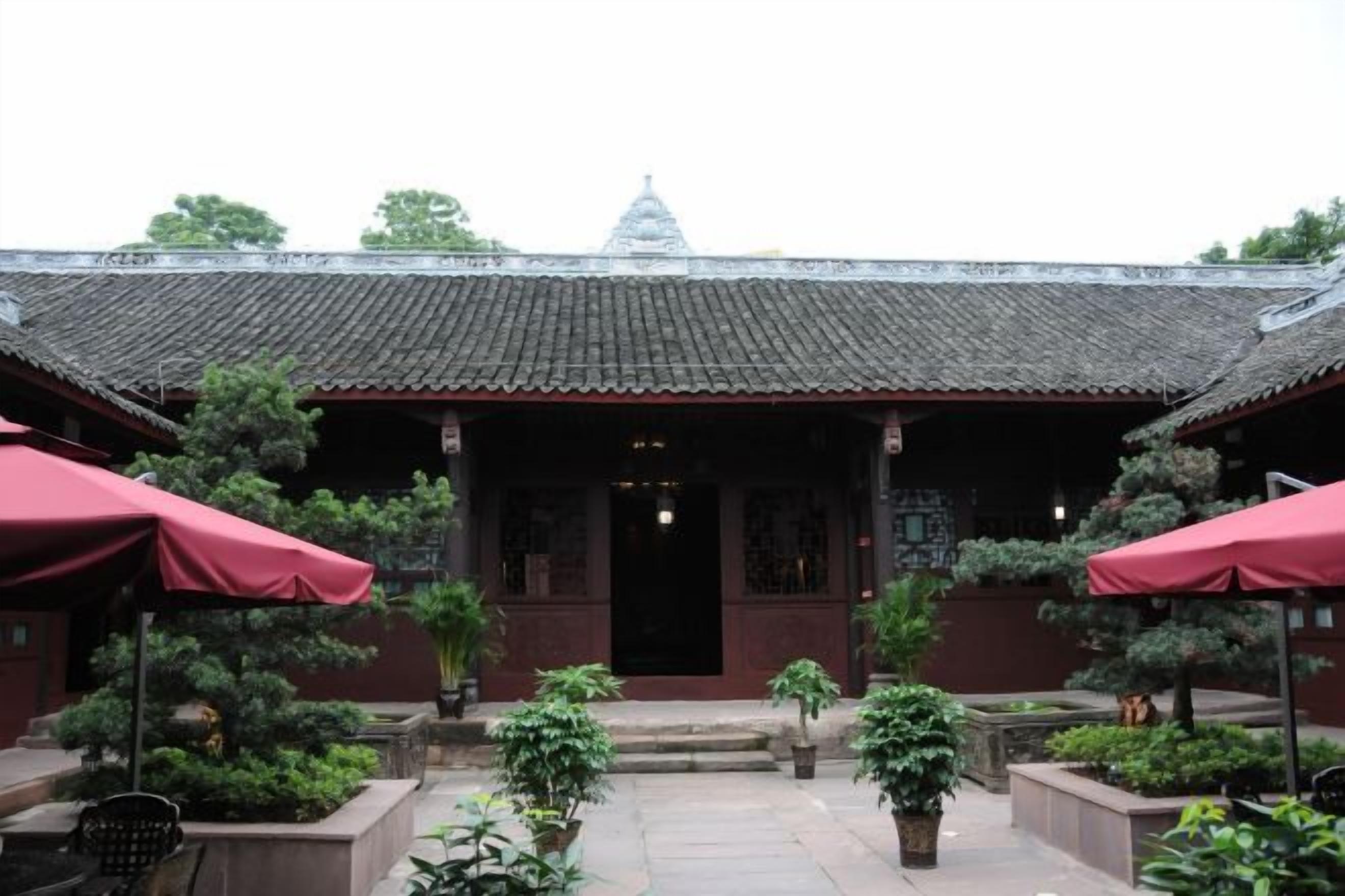 A traditional building with a tiled roof, a central entrance, and potted plants around the entrance area.