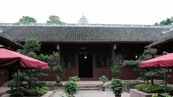 A traditional building with a tiled roof, a central entrance, and potted plants around the entrance area.
