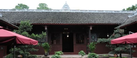 A traditional building with a tiled roof, a central entrance, and potted plants around the entrance area.