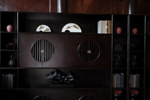 Um armário de madeira escura com recortes circulares, prateleiras com livros e objetos decorativos.
