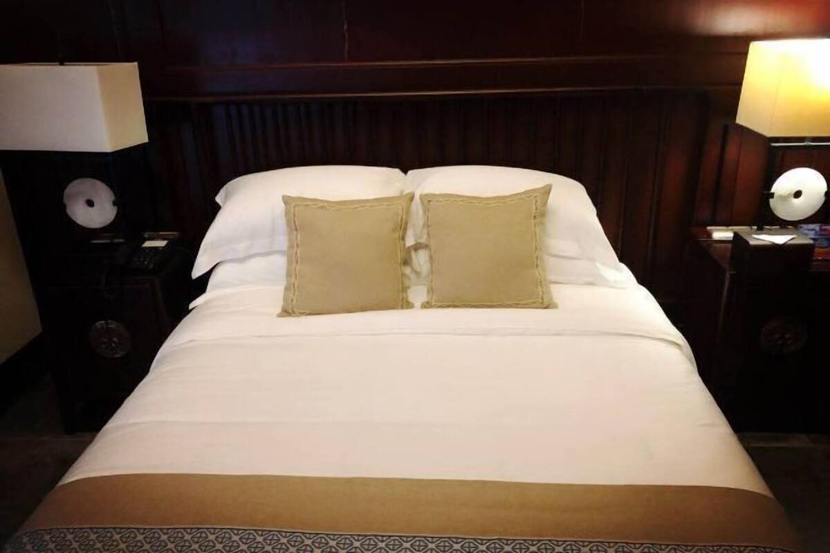 A neatly made bed with white linens and two beige pillows, flanked by two bedside tables with lamps, in a dimly lit room.