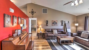 A living room with a red accent wall, a piano, a brown leather sofa, and a coffee table.