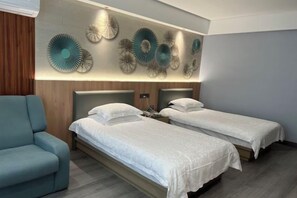 A hotel room with two single beds, a blue armchair, and decorative wall art. - Gutang Hotel (Yuyao)