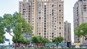 Un edificio residencial de varios pisos con balcones, rodeado de árboles y una calle con comercios.