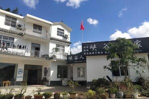 A traditional building with a red flag, a signboard with Chinese characters, and potted plants in the courtyard. - Xiagu Renjia Hostel (Qianshan)