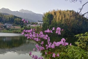 A serene lakeside view with mountains in the background and a building with a modern design near the water. - Xiagu Renjia Hostel (Qianshan)