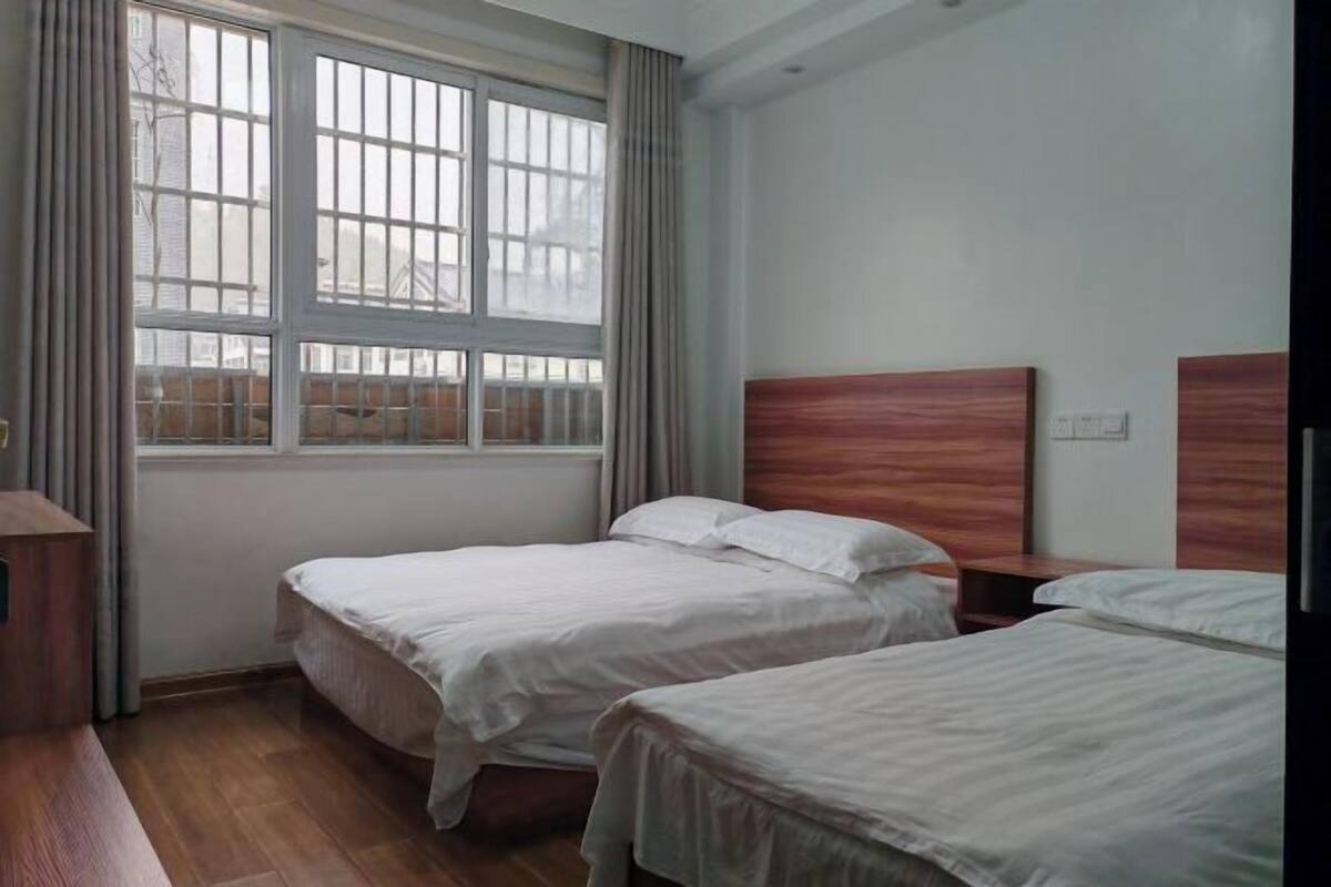A room with two beds, a window with curtains, and a wooden headboard.