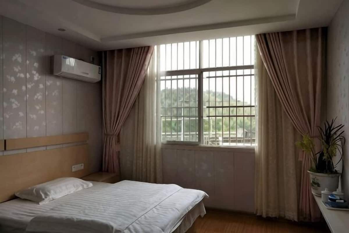 A bedroom with a bed, window, curtains, and a potted plant.