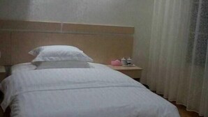 Una cama individual con cabecera de madera, una mesita de noche con lámpara y una ventana con cortinas de encaje.
