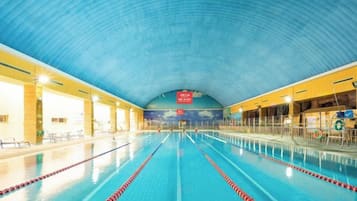 An indoor swimming pool with clear lanes, a high arched ceiling, and a mural on the wall.
