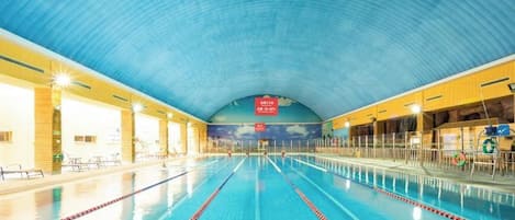 An indoor swimming pool with clear lanes, a high arched ceiling, and a mural on the wall.