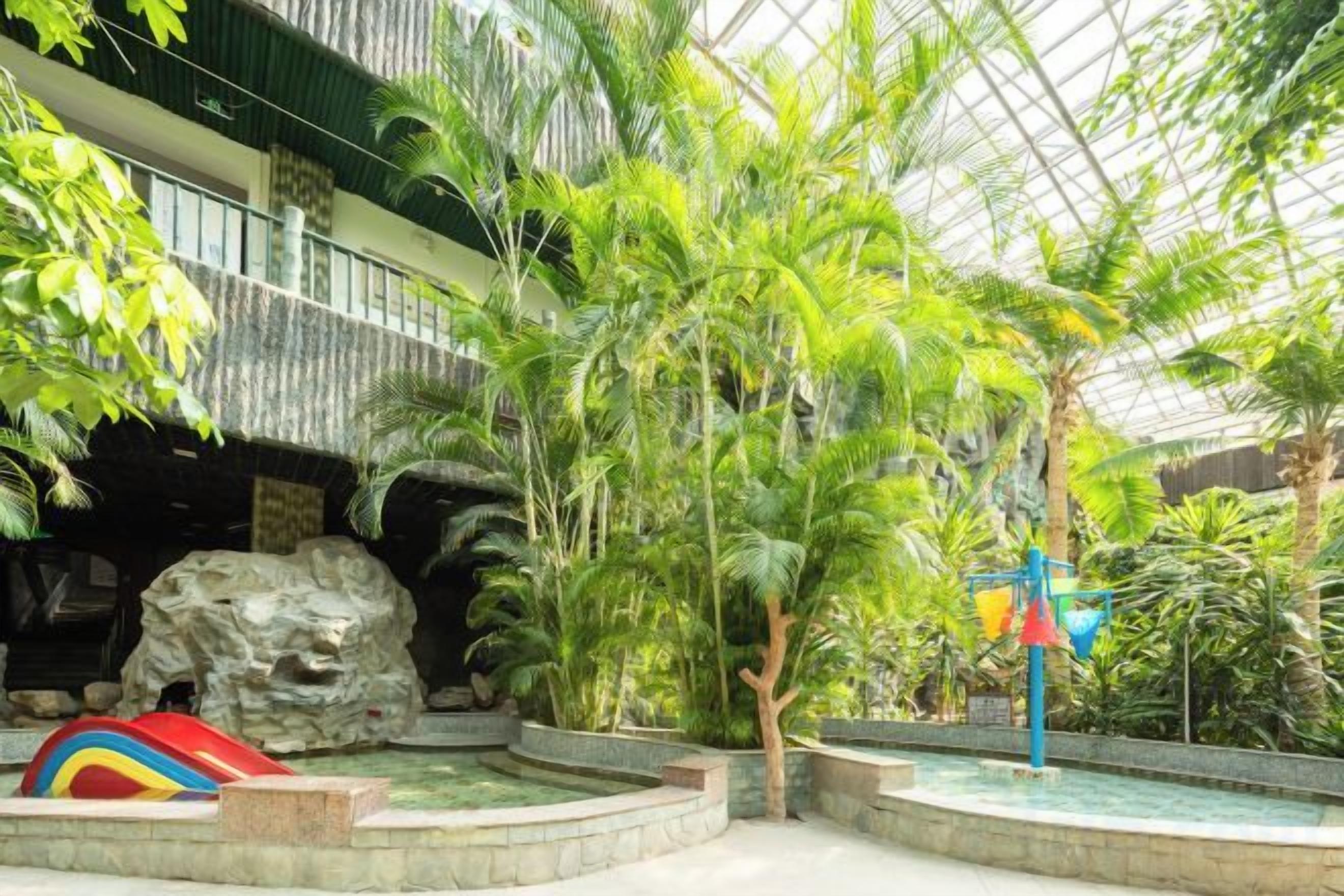 Un atriumo interior con una formación rocosa, palmeras y una estructura de juegos colorida.