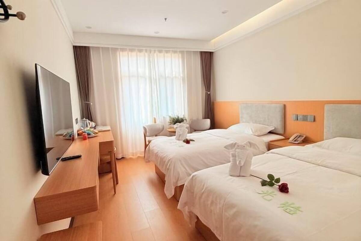 Une chambre d’hôtel avec deux lits, un bureau, une télévision et une fenêtre avec des rideaux.