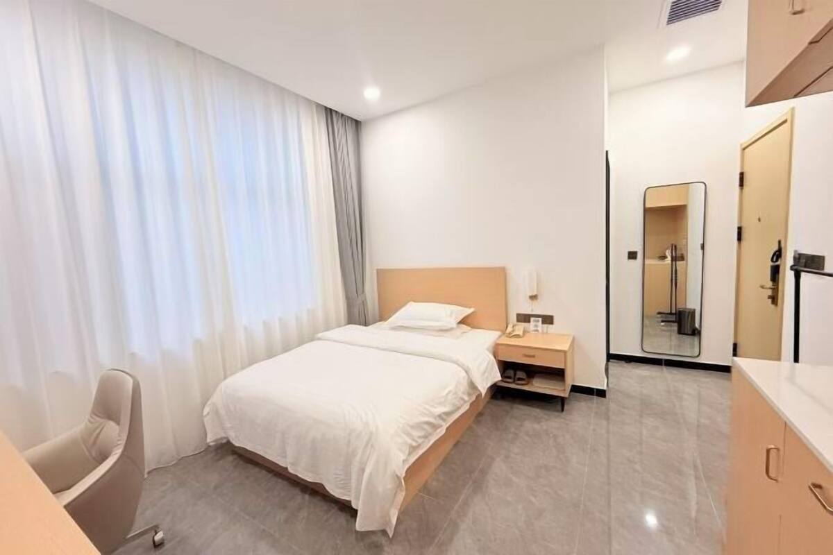 Une chambre d’hôtel avec un lit, une table de chevet, une chaise et un miroir.