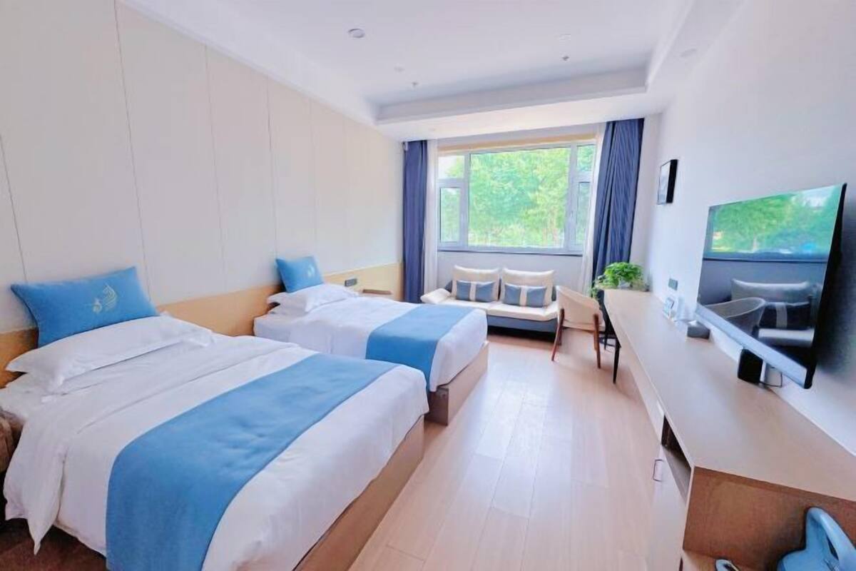Une chambre d’hôtel avec deux lits, une télévision, un bureau et une fenêtre avec des rideaux.