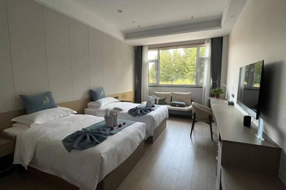 Une chambre d’hôtel avec deux lits, un bureau, une télévision et une fenêtre donnant sur un paysage verdoyant.