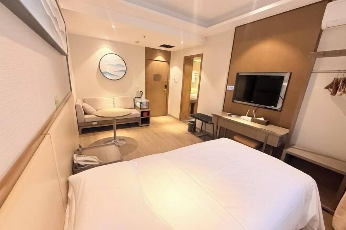 Une chambre d’hôtel comprenant un lit, un bureau, une chaise, un téléviseur fixé au mur et un miroir rond.