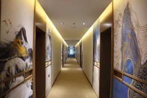 A hotel corridor with a carpeted floor, wooden doors, and walls adorned with abstract art.