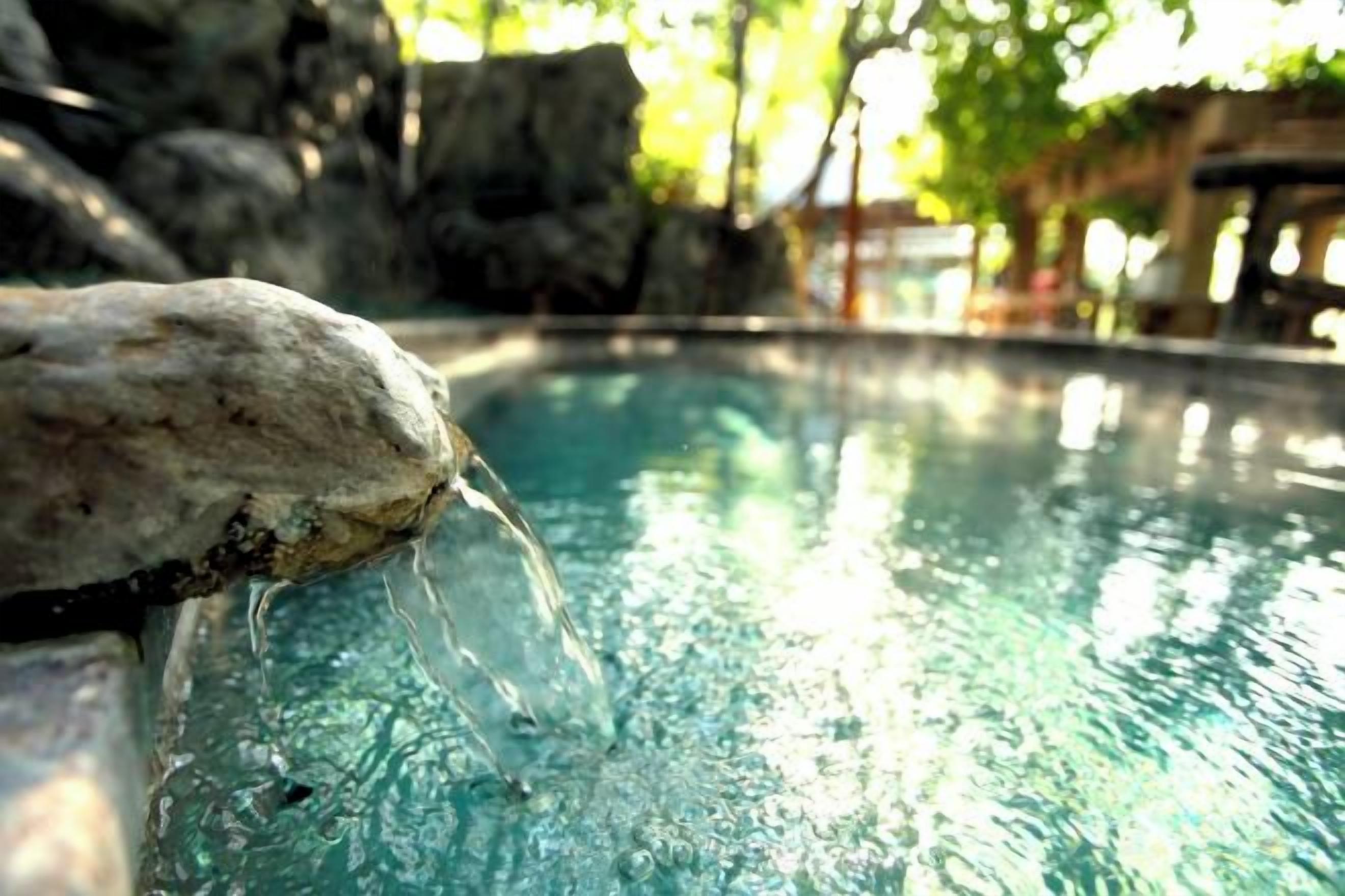 A clear pool with water flowing over rocks, surrounded by a natural landscape.