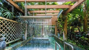 Een waterpartij met waterval over treden, omringd door weelderig groen en houten constructies.