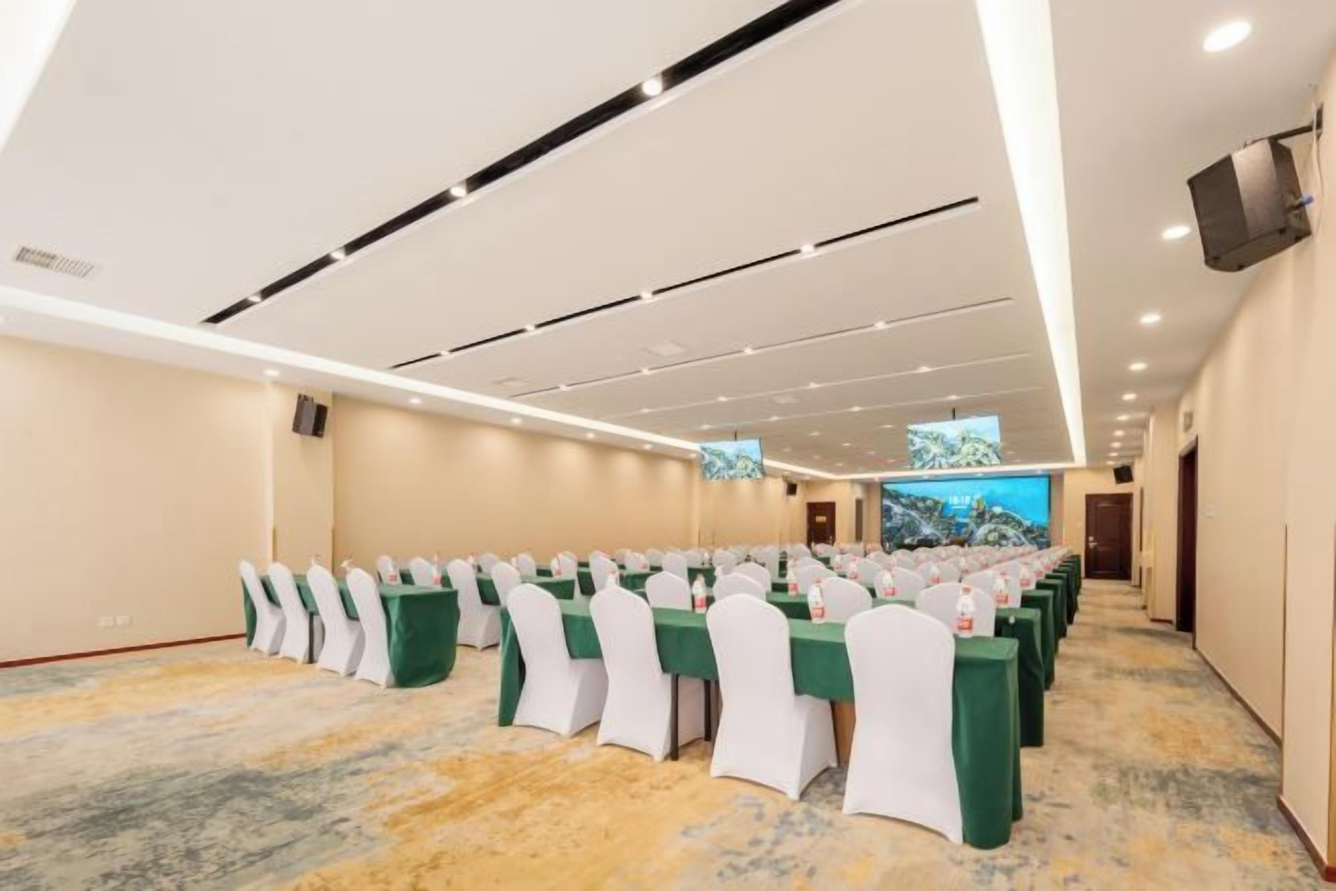 A conference room with rows of tables and chairs, a flat-screen TV, and a carpeted floor.
